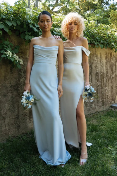 Two women in elegant Sawyer Bridesmaid Dresses by Jenny Yoo with off-the-shoulder sleeves, holding bouquets from Bergamot Bridal.