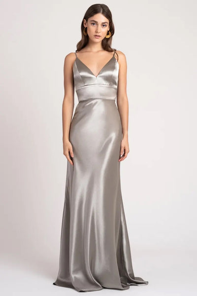 Woman modeling the Brenna - Bridesmaid Dress by Jenny Yoo, a silver satin back crepe fabric evening gown with a v-neckline and spaghetti straps from Bergamot Bridal.