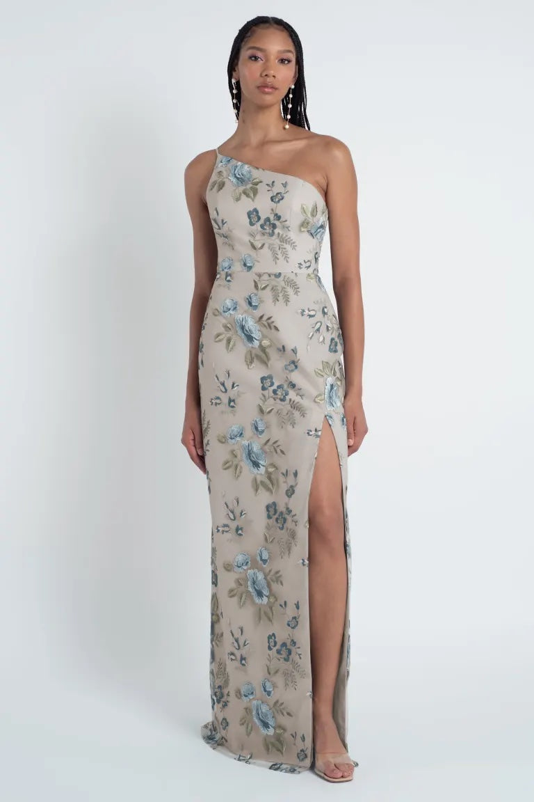 Woman posing in an enchanted floral print one-shoulder Jenny Yoo Bridesmaid Dress gown with a thigh-high slit.