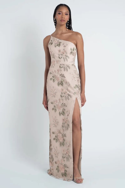 A woman in an elegant, embroidered tulle Jenny Yoo Bridesmaid Dress Bristol gown with a thigh-high slit stands poised against a neutral background.