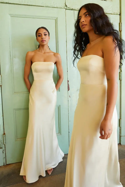 Two women in elegant strapless dresses with a bias cut skirt, posing by a green door wearing Melody bridesmaid dresses by Jenny Yoo from Bergamot Bridal.