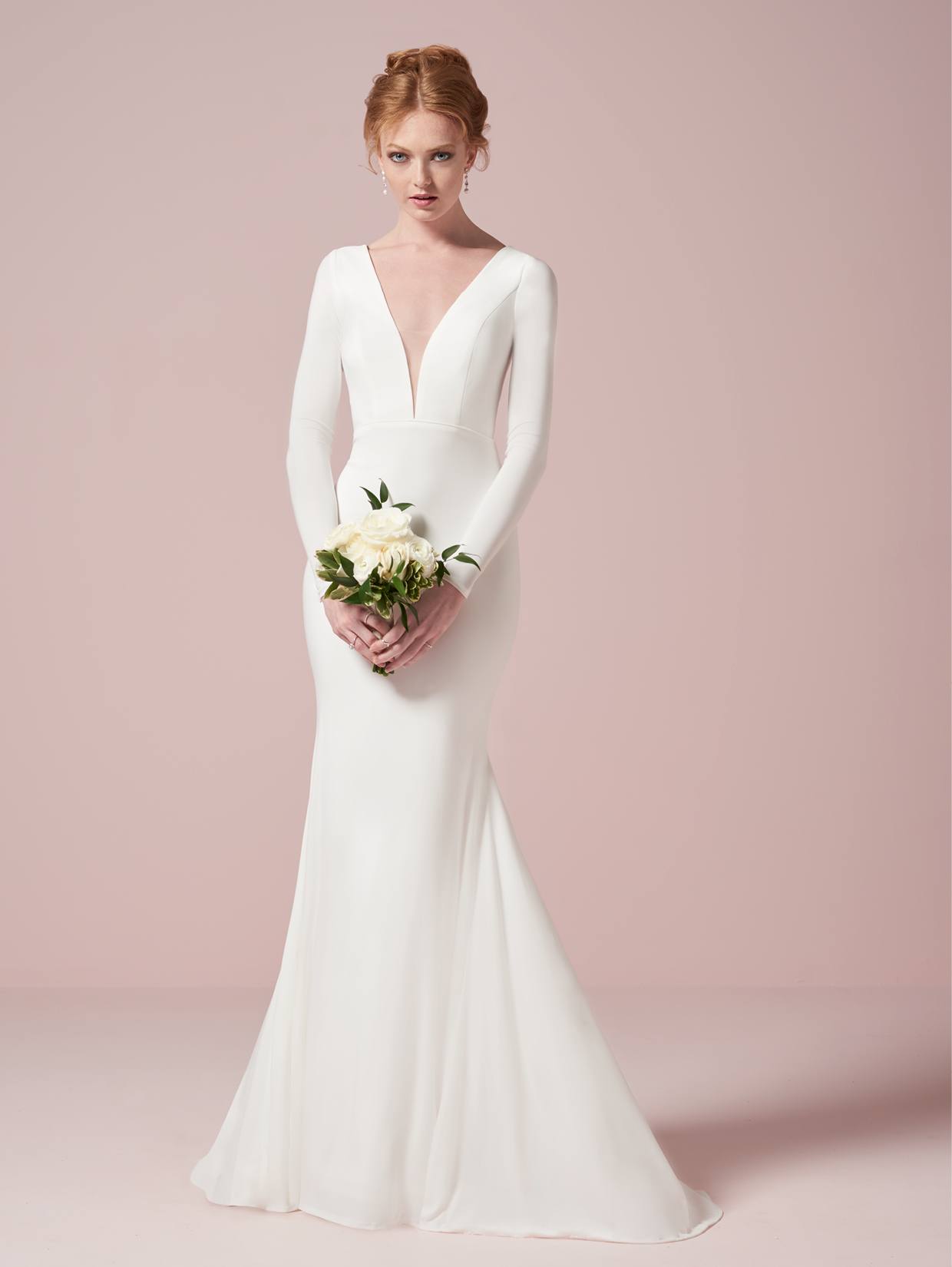 Dressed in the Simple Long Sleeve Bridal Gown by Christina Wu, available at Bergamot Bridal and featuring a plunging neckline, a person holds a bouquet of white flowers against a plain background.