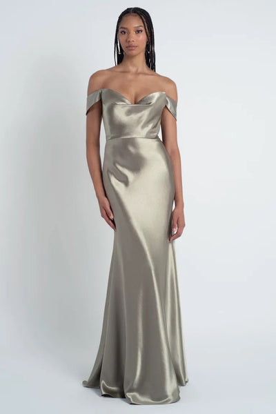 A woman wearing a strapless, off-the-shoulder silver Camilla - Bridesmaid Dress by Jenny Yoo with a sculpted cowl sweetheart neck poses against a plain white background, sold by Bergamot Bridal.