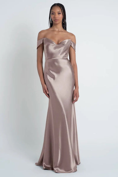 A person wearing a strapless, metallic, floor-length Camilla - Bridesmaid Dress by Jenny Yoo from Bergamot Bridal with a sculpted cowl sweetheart neck stands against a plain background.