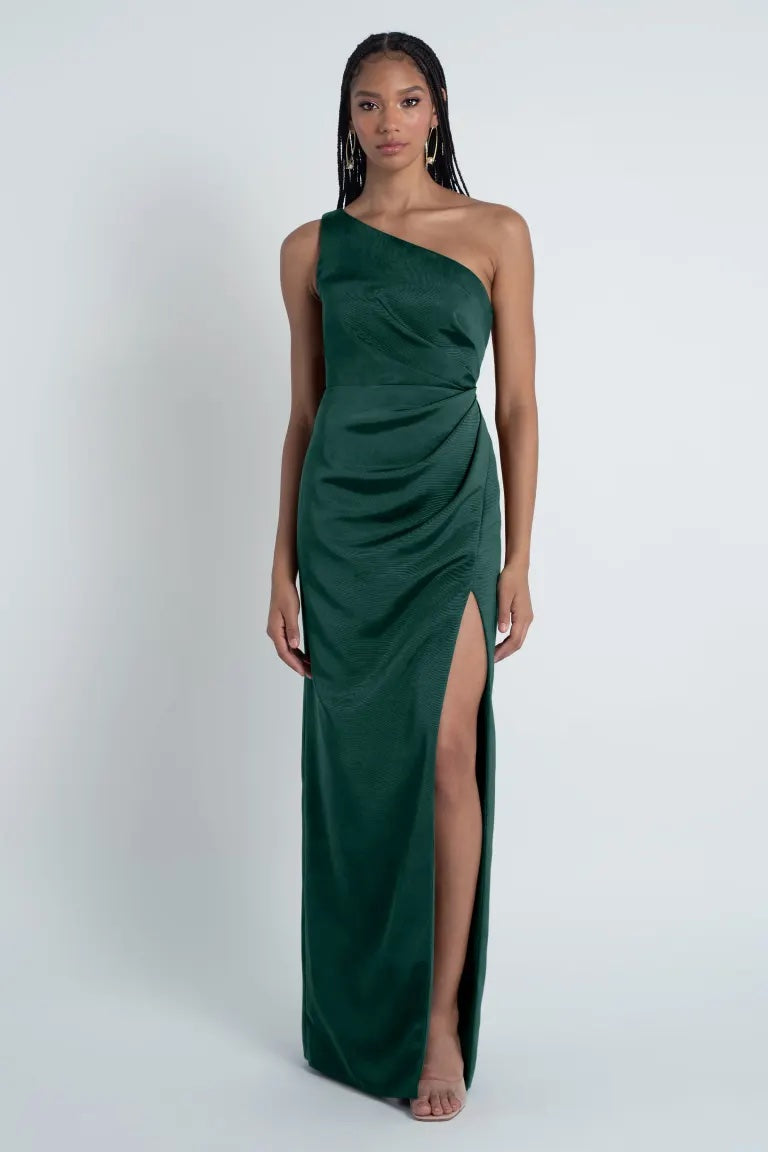 Woman posing in an elegant Jenny Yoo Bridesmaid Dress from Bergamot Bridal, crafted from Luxe Faille fabric, featuring a one-shoulder neckline and a high slit.