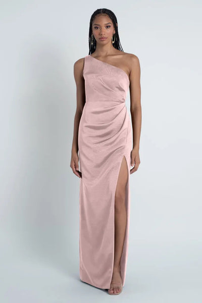 A woman wearing an elegant Jenny Yoo Bridesmaid Dress made of Luxe Faille fabric by Carolina, featuring a one-shoulder neckline with a high leg slit from Bergamot Bridal.