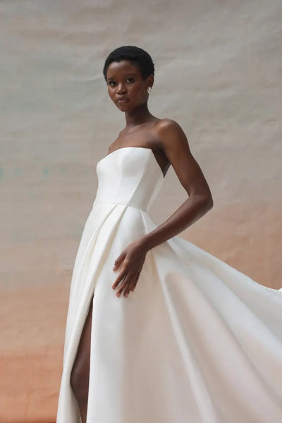 A person wearing a strapless white Catherine Wedding Dress by Jenny Yoo from Bergamot Bridal poses against a neutral background, exuding Hollywood glamour.