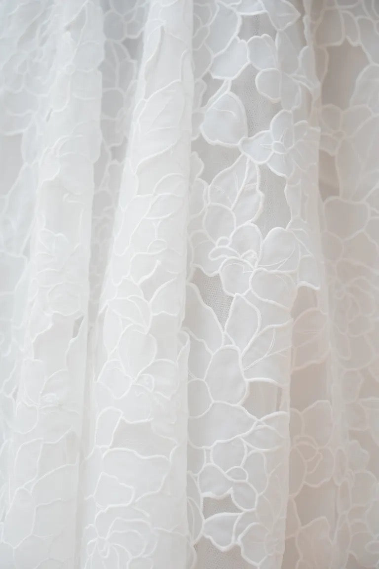 Close-up of a white lace fabric with a floral organza pattern, reminiscent of the intricate details found on the Charlie Wedding Dress by Jenny Yoo, available at Bergamot Bridal.