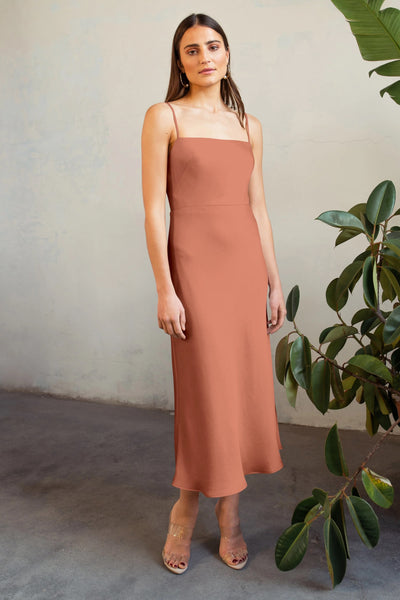 Woman in a Claudia Bridesmaid Dress by Jenny Yoo, standing next to a plant, against a textured wall.