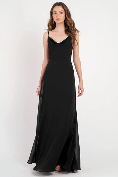 A woman posing in a simple black slip dress with a cowl neckline, the Colby - Jenny Yoo Bridesmaid Dress from Bergamot Bridal.