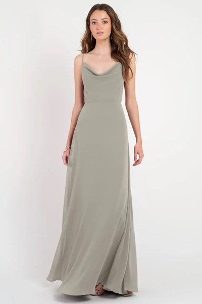 A woman in an elegant, full-length, cowl neckline, sage green Colby - Jenny Yoo Bridesmaid Dress stands against a white background from Bergamot Bridal.
