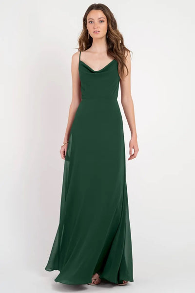 A woman modeling a floor-length green Colby - Jenny Yoo Bridesmaid Dress with a cowl neckline from Bergamot Bridal.