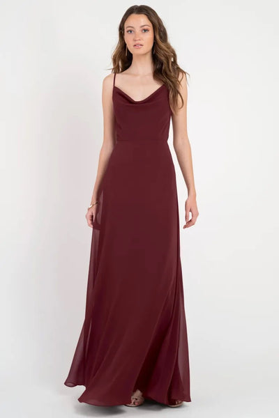 Woman in a burgundy Colby - Jenny Yoo bridesmaid dress with a cowl neckline standing against a plain background from Bergamot Bridal.