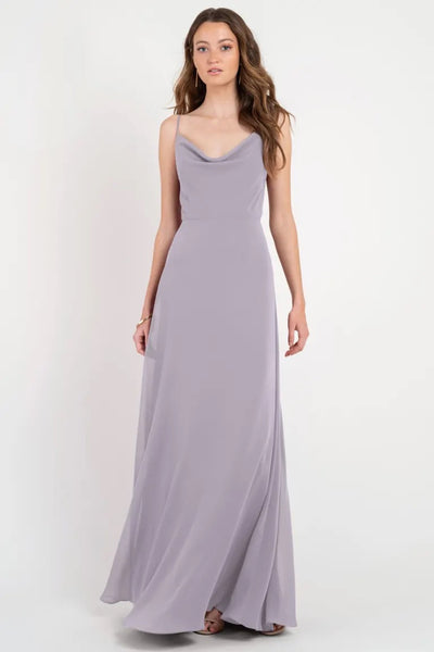 Woman in a long, flowing, gray Colby Jenny Yoo Bridesmaid Dress standing against a white background from Bergamot Bridal.