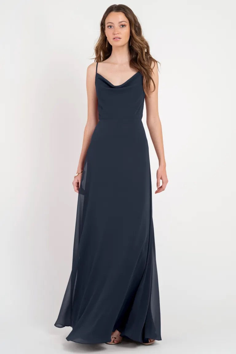 A woman posing in a Colby - Jenny Yoo Bridesmaid Dress evening gown in navy blue with a cowl neckline.
