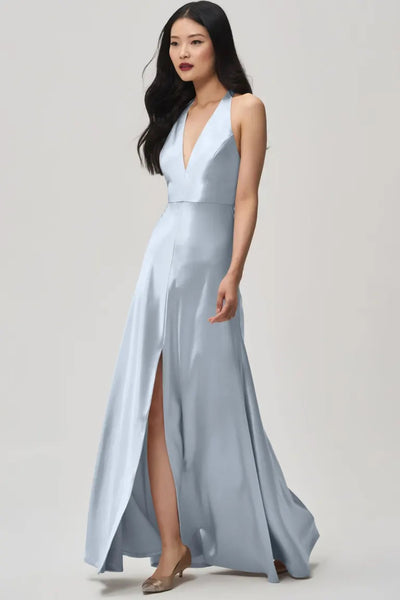 A woman in the Corinne - Bridesmaid Dress by Jenny Yoo Off The Rack from Bergamot Bridal, boasting a plunging halter V-neck and slit design, walks confidently.