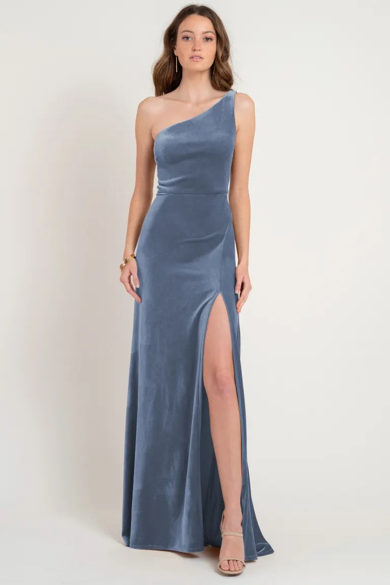 Woman posing in an elegant Cybill - Bridesmaid Dress by Jenny Yoo, stretch velvet one-shoulder dress with a high leg slit from Bergamot Bridal.