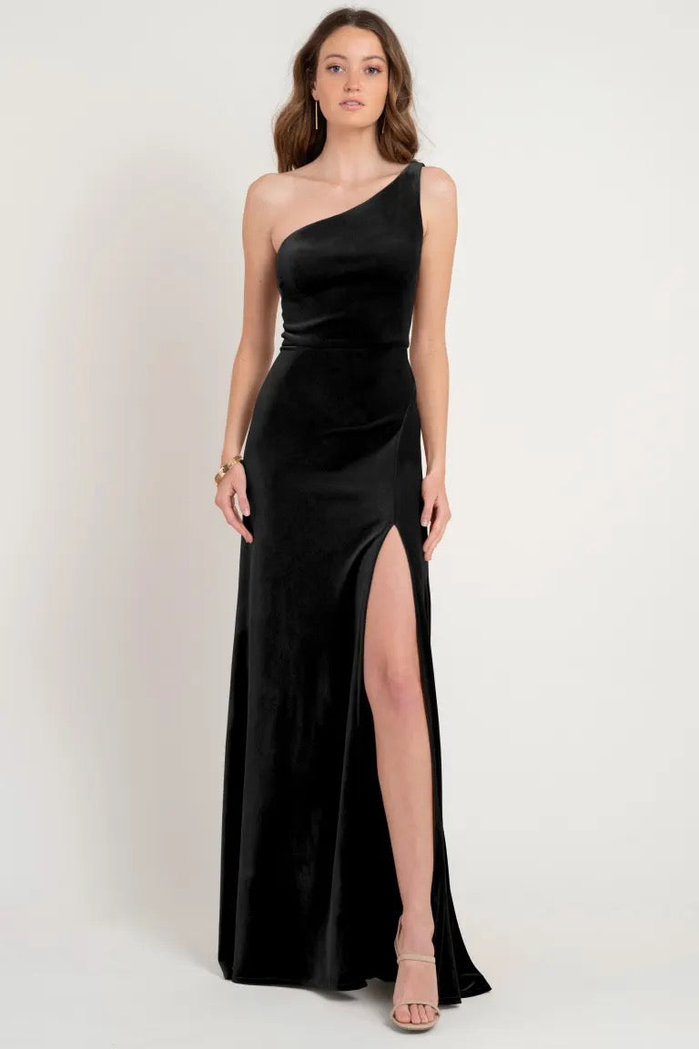 Woman wearing a Cybill - Bridesmaid Dress by Jenny Yoo sample size 12, one-shoulder black evening gown made of stretch velvet with a thigh-high slit from Bergamot Bridal.