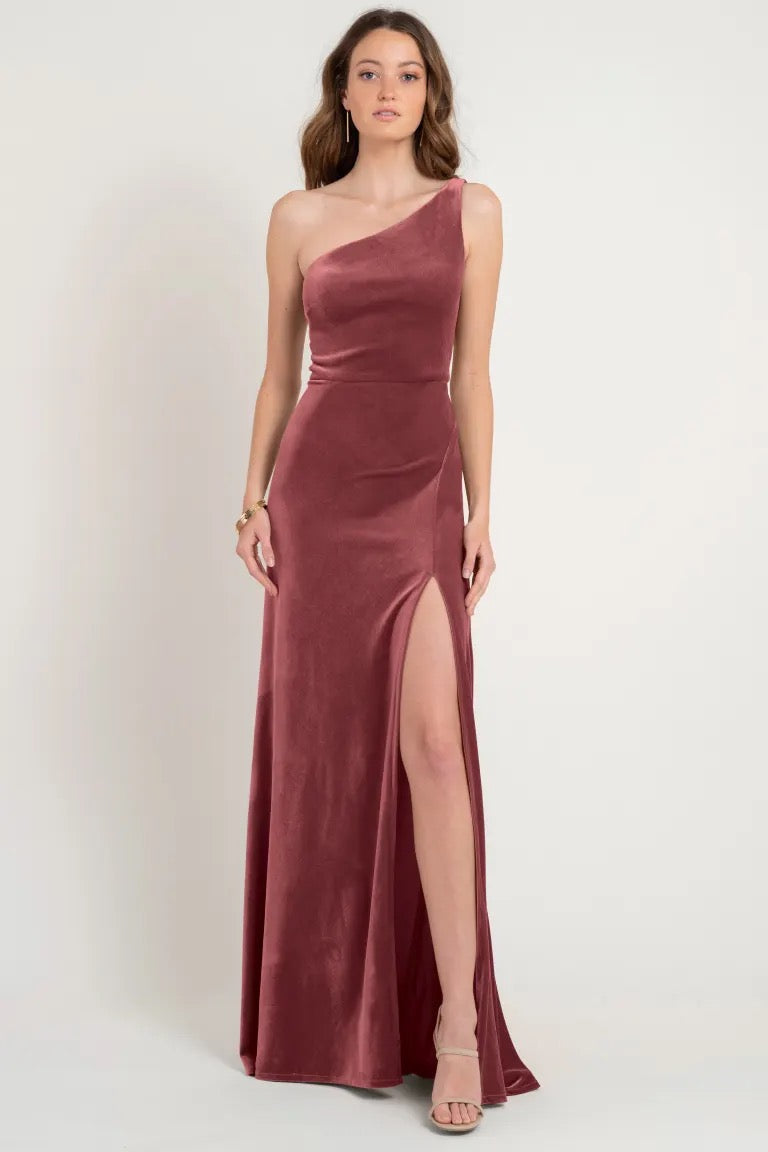 Woman in an elegant one-shoulder maroon stretch velvet gown with a high slit, sample size 12, the Cybill Bridesmaid Dress by Jenny Yoo at Bergamot Bridal.