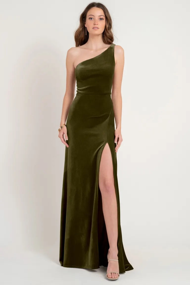 Woman in an elegant one-shoulder stretch velvet olive green gown with a thigh-high slit, Cybill - Bridesmaid Dress by Jenny Yoo, store sample size 12 from Bergamot Bridal.
