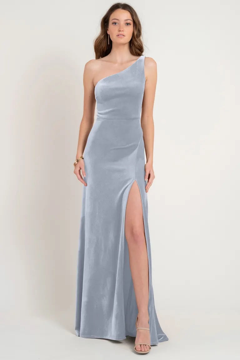 A woman modeling a store sample size 12, one-shoulder, silver evening gown crafted from Stretch Velvet with a thigh-high slit. The Cybill bridesmaid dress by Jenny Yoo at Bergamot Bridal.