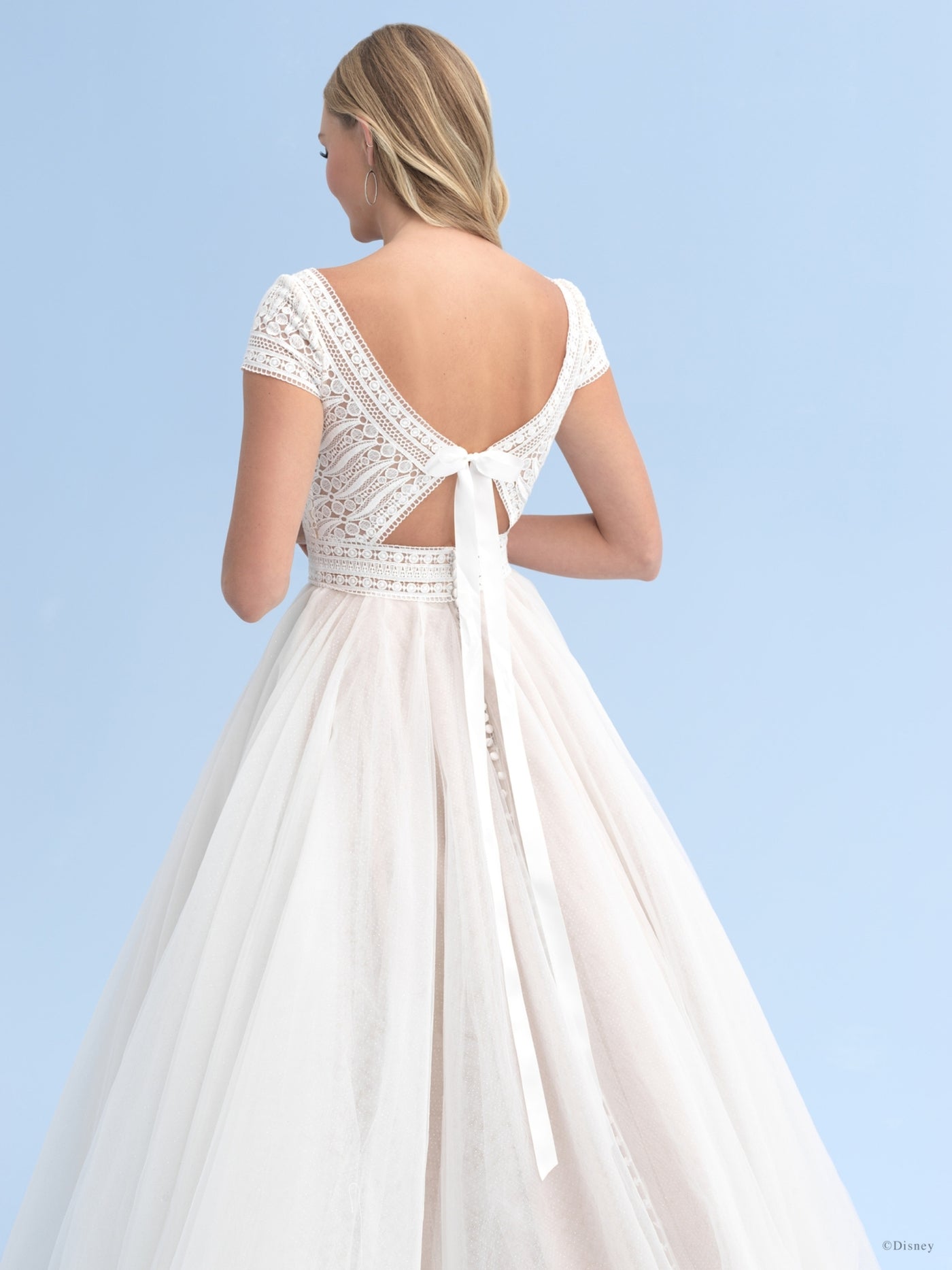 Woman in a Bergamot Bridal Allure Disney Wedding Dress - Rapunzel - Off The Rack with lace bodice and a low-cut back against a blue sky background.