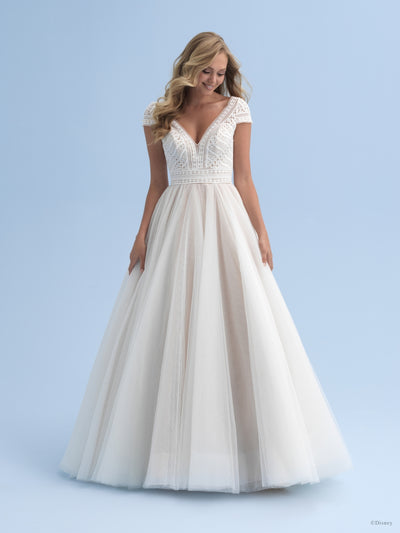 A woman in an elegant white Bergamot Bridal bridal ball gown with a beaded bodice and a voluminous swiss dot sparkle tulle skirt standing against a light blue background.
