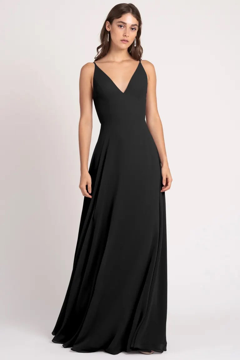 Woman posing in the Dani Bridesmaid Dress by Jenny Yoo from Bergamot Bridal, an elegant black evening gown with a v-neckline and sharp tailoring.
