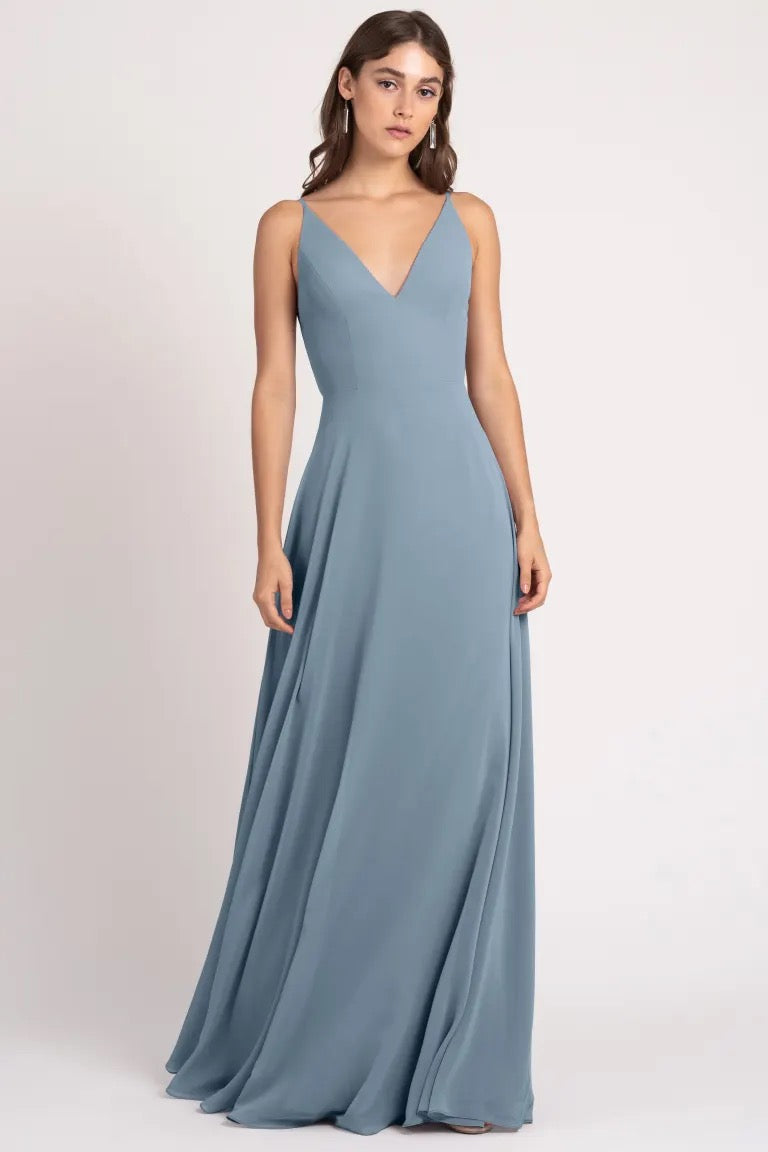 A woman wearing an elegant blue Dani - Bridesmaid Dress by Jenny Yoo a-line silhouette gown with a v-neckline from Bergamot Bridal.