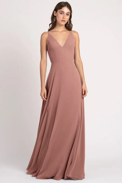 A woman modeling a long, elegant, dusty rose-colored Dani - Bridesmaid Dress by Jenny Yoo with a v-neckline and a keyhole back from Bergamot Bridal.