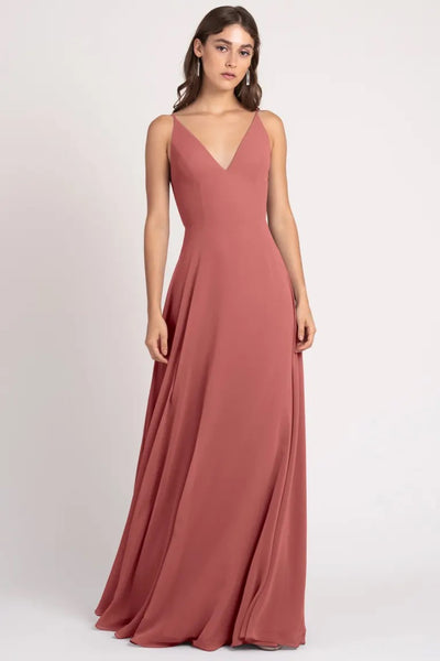 Woman in an elegant a-line silhouette, sleeveless rose-colored Dani - Bridesmaid Dress by Jenny Yoo gown with a v-neckline and keyhole back from Bergamot Bridal.