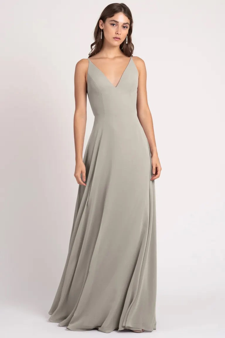 Woman modeling a floor-length, sleeveless, v-neck evening gown with a keyhole back in a neutral tone by Bergamot Bridal.