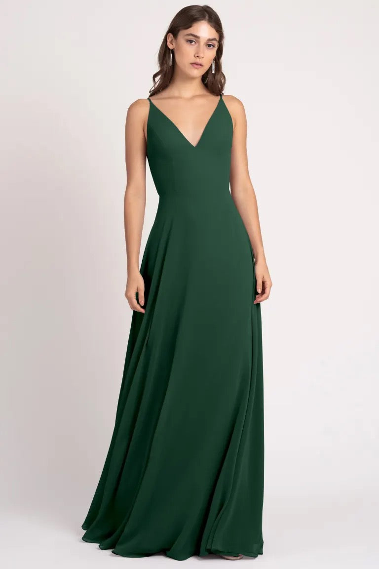 A woman in an elegant Dani bridesmaid dress by Jenny Yoo from Bergamot Bridal stands against a neutral backdrop.