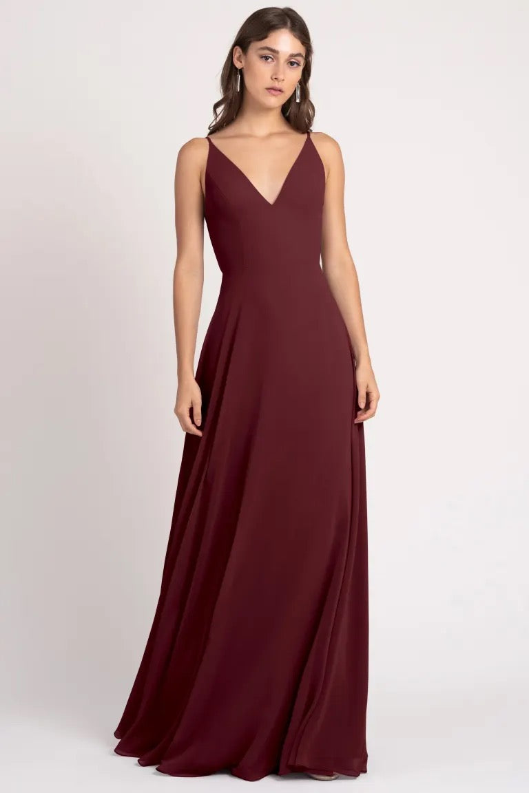 A woman in an elegant burgundy evening gown with a v-neckline and a keyhole back, the Dani Bridesmaid Dress by Jenny Yoo from Bergamot Bridal.