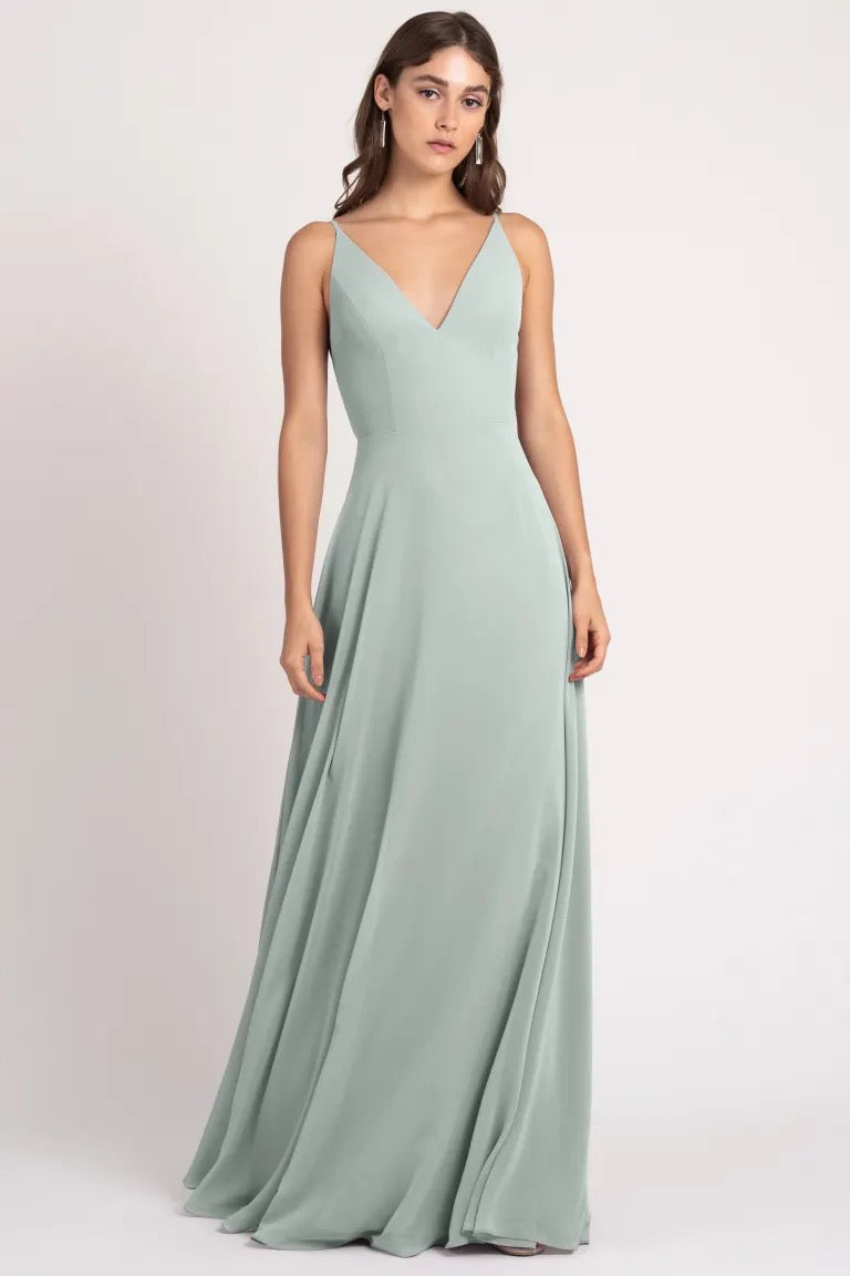 Woman in a sage green evening gown with a sharp tailoring v-neckline and an A-line silhouette, wearing the Dani bridesmaid dress by Jenny Yoo from Bergamot Bridal.