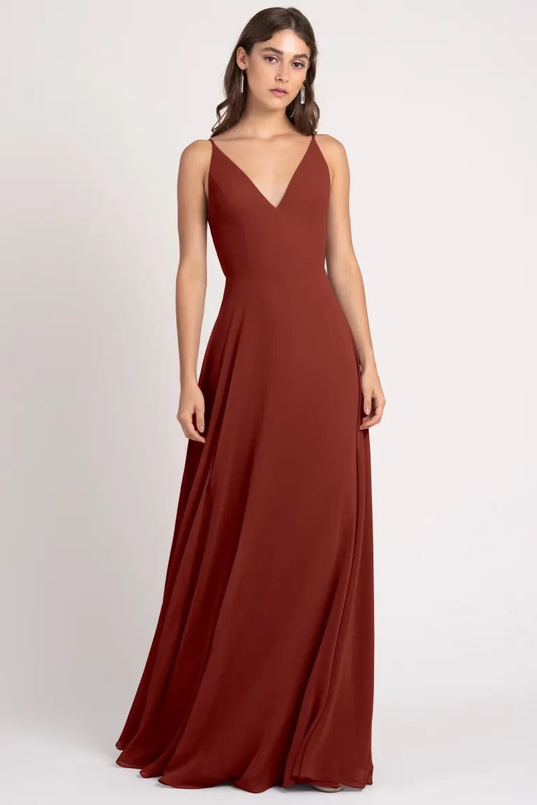 A woman wearing a sleeveless, v-neck, rust-colored evening gown with sharp tailoring, the Dani-Bridesmaid Dress by Jenny Yoo from Bergamot Bridal.
