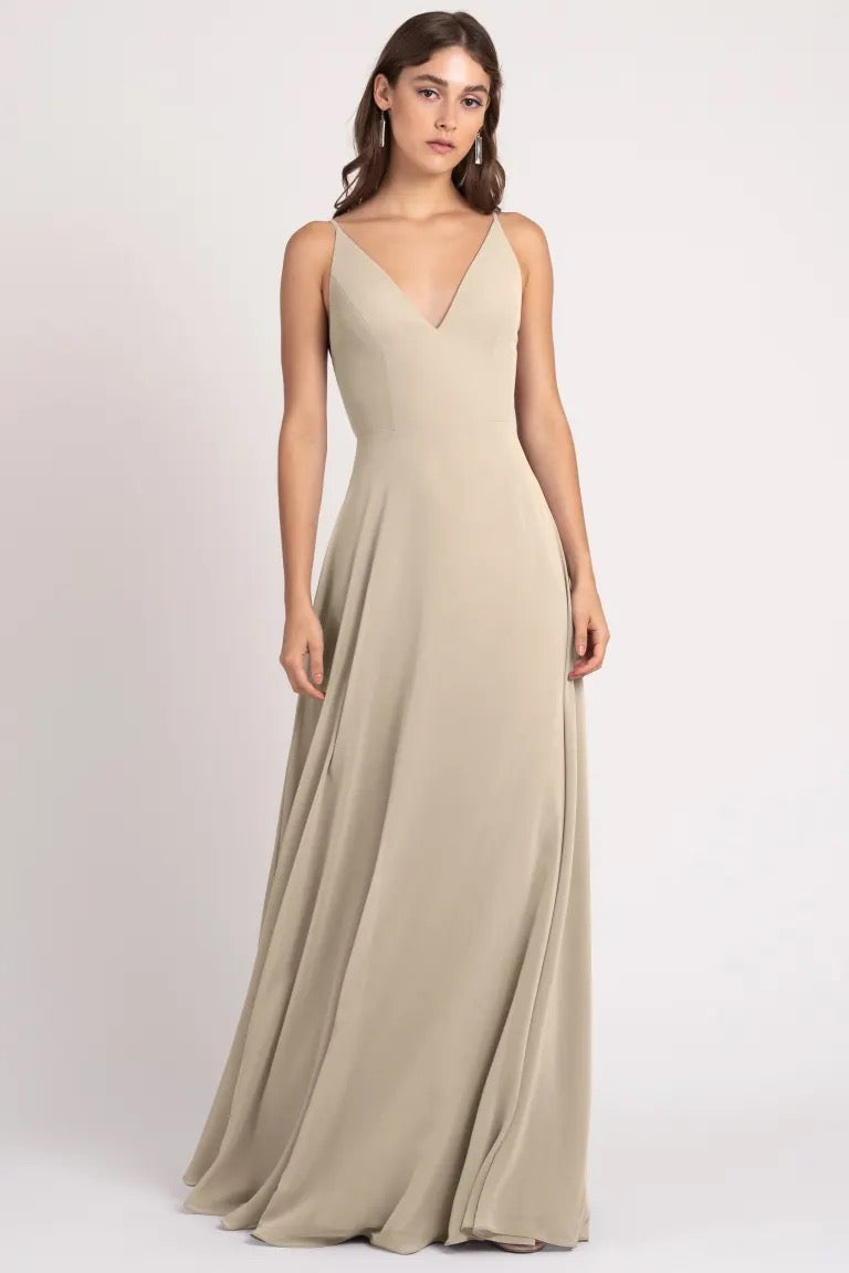 Woman posing in an elegant beige evening gown with a v-neckline and a keyhole back, the Dani Bridesmaid Dress by Jenny Yoo from Bergamot Bridal.