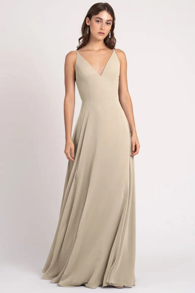 Woman posing in an elegant beige evening gown with a v-neckline and a keyhole back, the Dani Bridesmaid Dress by Jenny Yoo from Bergamot Bridal.