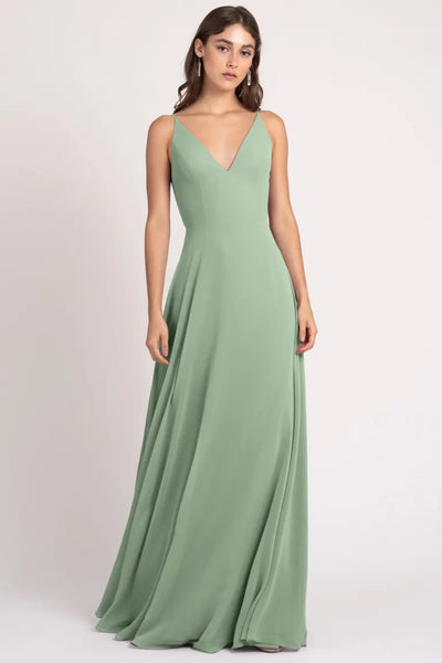 A woman in an elegant green sleeveless Dani - Bridesmaid Dress by Jenny Yoo with a v-neckline and a keyhole back from Bergamot Bridal.