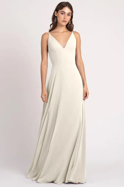 A woman wearing an elegant cream evening gown with a v-neckline and a keyhole back, the Dani bridesmaid dress by Jenny Yoo from Bergamot Bridal.