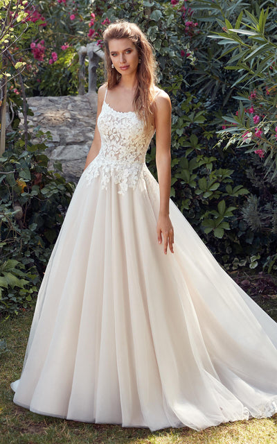 A woman posing outdoors in an elegant strapless Eddy K Daphne gown with floral appliqué on the bodice from Bergamot Bridal.