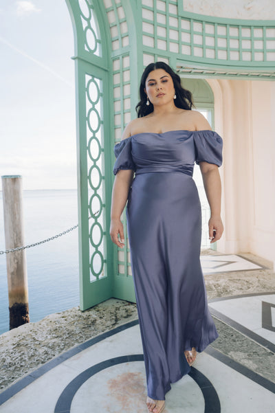 Woman in a Jenny Yoo Bridesmaid Dress with puff sleeves posing by a seaside pavilion.