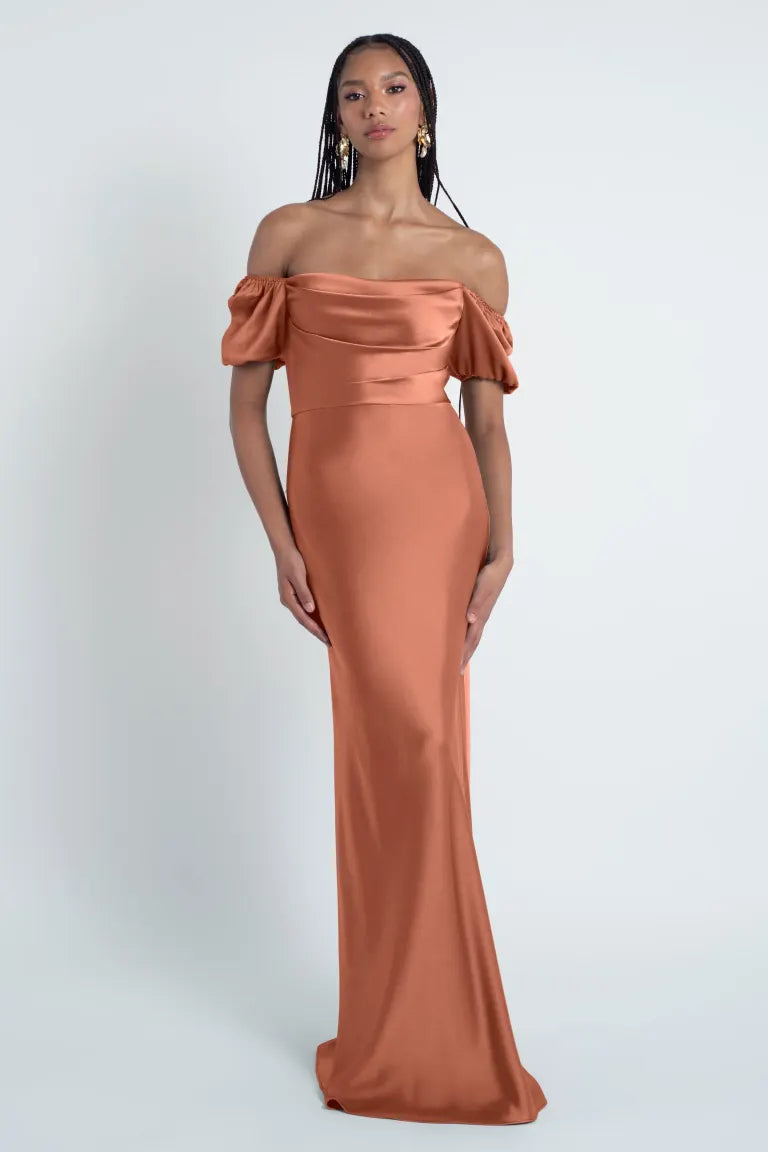 Woman in an elegant off-shoulder peach gown featuring a bias-cut skirt made from luxe satin fabric, known as the Eliana - Jenny Yoo Bridesmaid Dress from Bergamot Bridal.