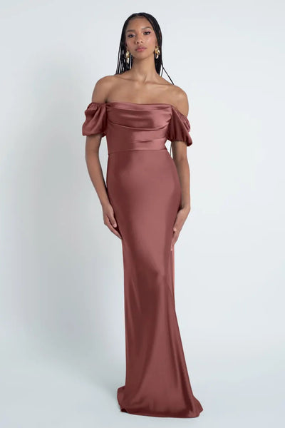 A woman in an elegant off-the-shoulder Jenny Yoo Bridesmaid Dress, featuring a rose-colored satin fabric from Bergamot Bridal.