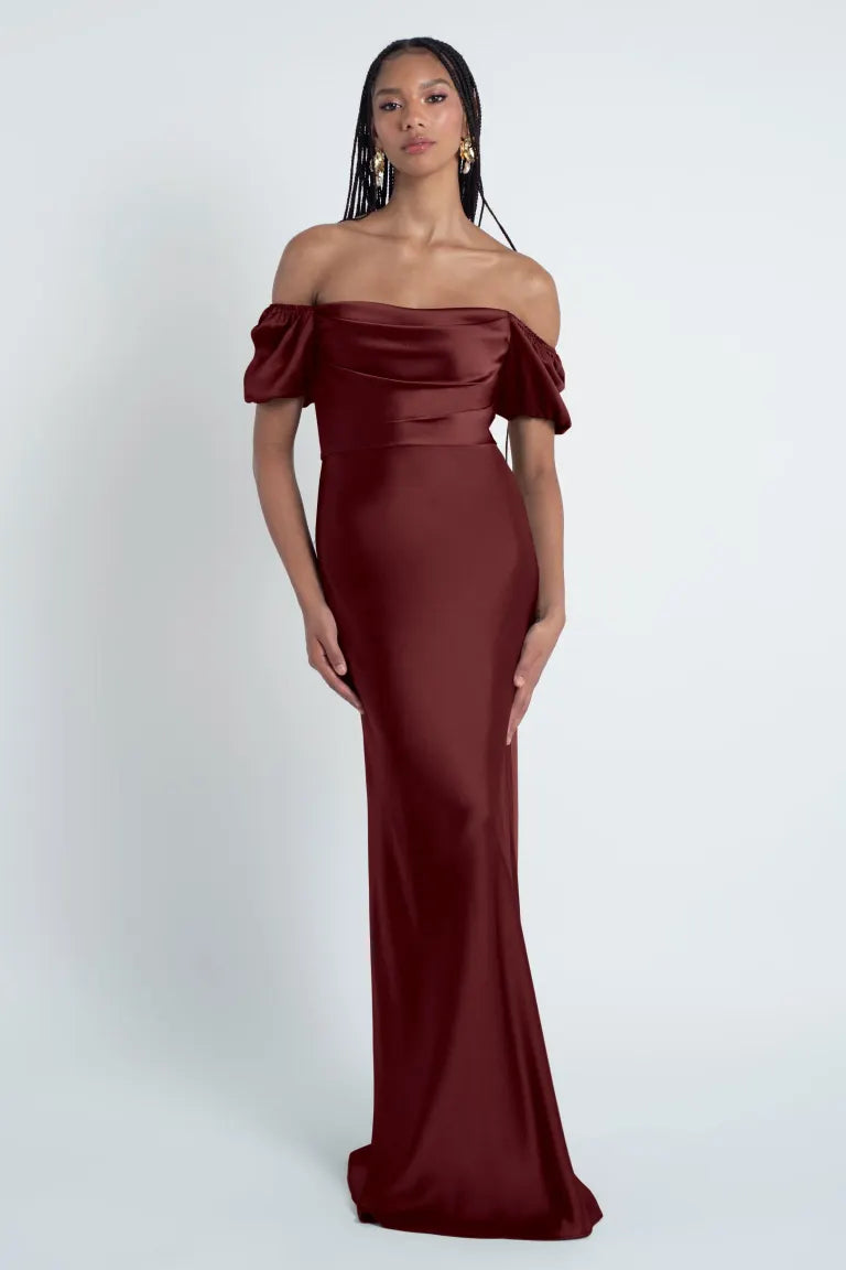 Woman posing in an elegant, Jenny Yoo Bridesmaid Dress off-the-shoulder, burgundy evening gown with a luxe satin fabric from Bergamot Bridal.