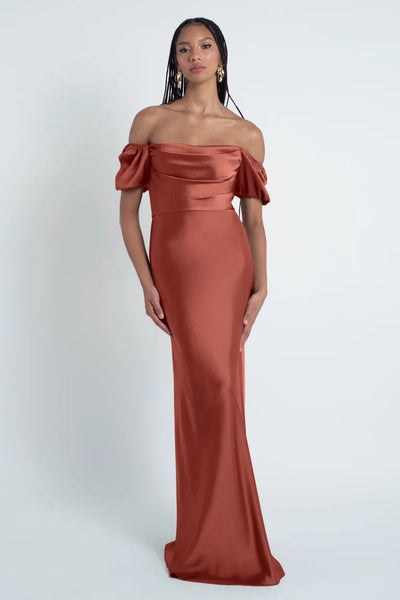 A woman in a luxe satin fabric Jenny Yoo Bridesmaid Dress with puff sleeves posing against a plain background.