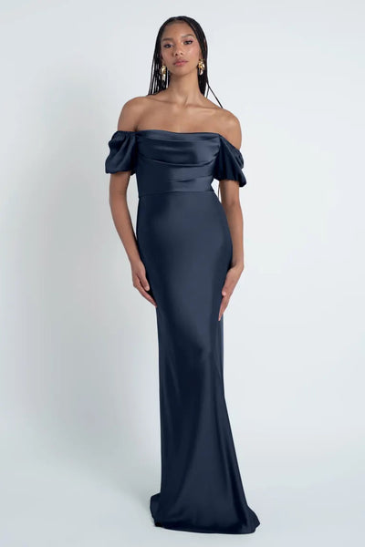 Woman in a Jenny Yoo Bridesmaid Dress crafted from luxe satin fabric, featuring an off-shoulder bias-cut skirt and a navy blue gown posing against a light background.