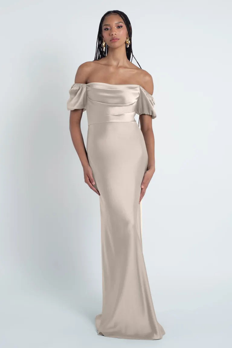 A woman modeling a sleek, Jenny Yoo Bridesmaid Dress with an off-shoulder style in luxe satin fabric by Bergamot Bridal.