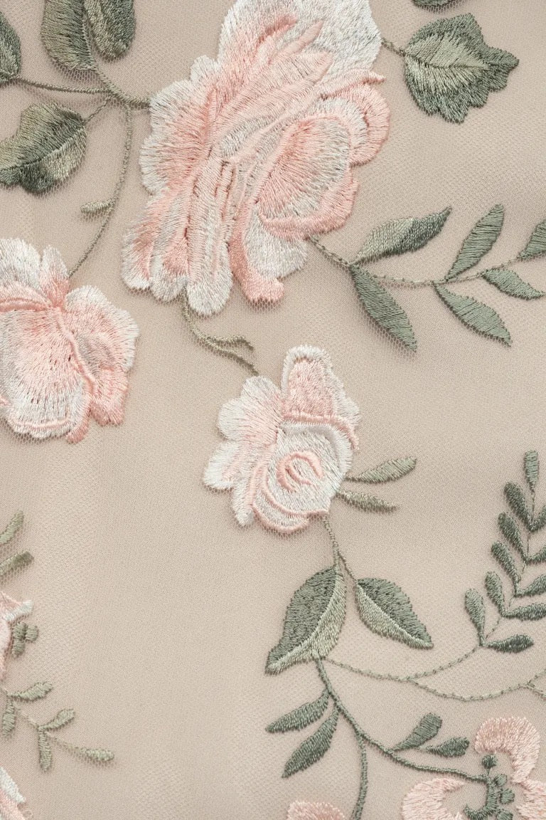 Close-up of an embroidered floral pattern with pink and white flowers and green leaves on a beige fabric background, perfect for the romantic Julianna Bridesmaid Dress by Jenny Yoo, available from Bergamot Bridal.