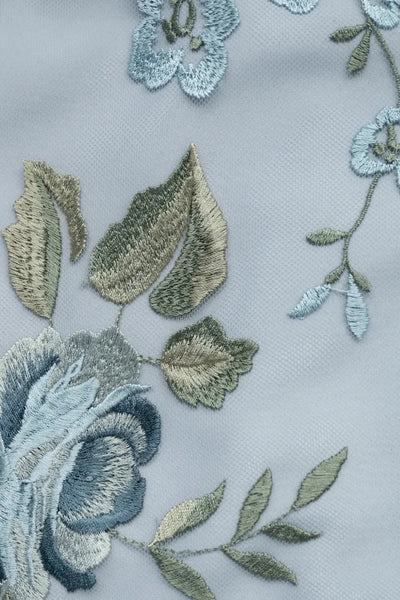 Embroidered enchanted floral tulle with blue flowers and green leaves on a light fabric background on the Drew Jenny Yoo Bridesmaid Dress by Bergamot Bridal.